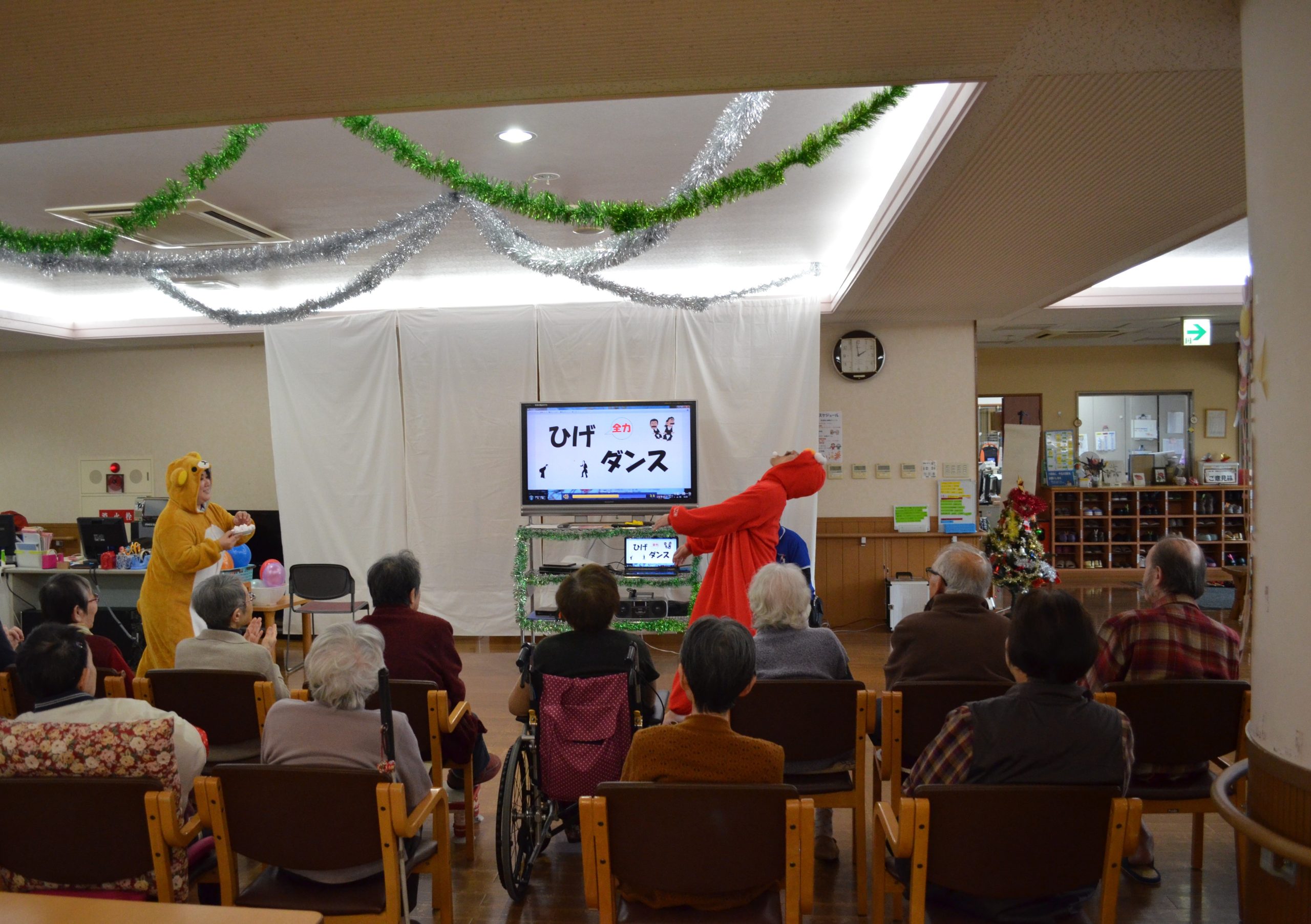 介護施設のクリスマス行事。入居者がステージの演技を鑑賞している様子。